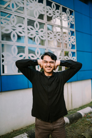 A young man blocking his ears with hands, showing distress and annoyance about loud noise in an urban settingの写真素材