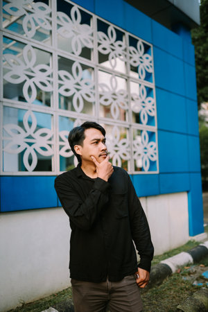 Young man thoughtfully considers options near a uniquely designed building. Contemplative mood conveys focus and strategic thinking.の写真素材