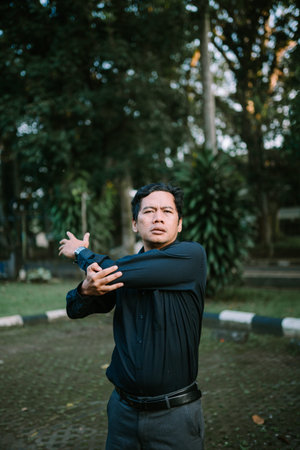 Man stretching his arm in the park. Outdoor activity for health, wellness and fitness concept. Dark...