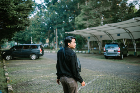 Thoughtful asian man standing in the outdoor parking lot. Man looking away in calm state.の写真素材