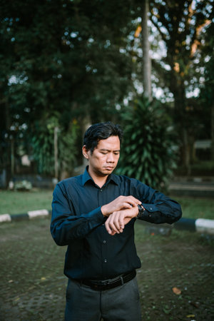 Business man in formal attire checking the time on his wristwatch in an outdoor setting, showing focusの写真素材