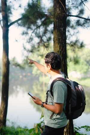 A man using a GPS map arrives at a scenic, cool lake during his travel, enjoying the refreshing atmosphere and natural beauty of the destination.の写真素材