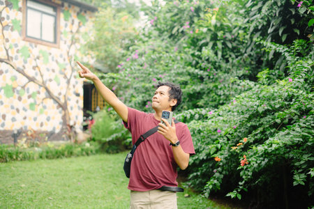 An excited man visits a peaceful villa surrounded by trees, capturing the moment with his phone as he records and takes selfies in the tranquil settingの写真素材