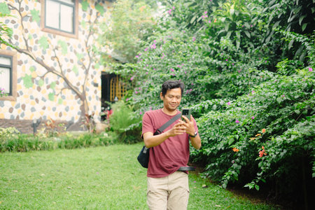 An excited man visits a peaceful villa surrounded by trees, capturing the moment with his phone as he records and takes selfies in the tranquil settingの写真素材