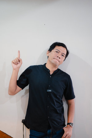 A portrait captures a man gesturing upwards with a finger raised, set against a neutral backdrop. His expression suggests thoughtful consideration, adding depth to the image. He is dressed in casualの写真素材