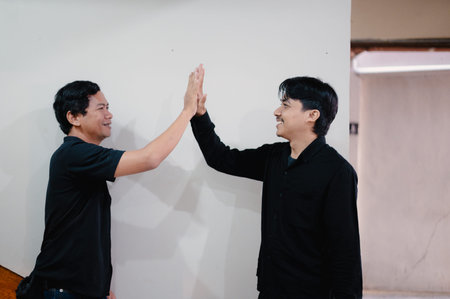 Two men celebrating a successful partnership with a high-five gesture of camaraderie and connection, showing mutual respect and support for their accomplishment in a positive environment.の写真素材