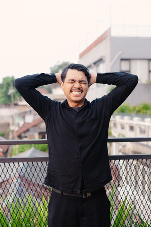 A man expresses distress by placing his hands behind his head, showcasing a strong emotional...