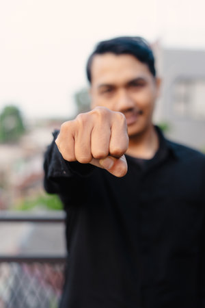 A man extends his clenched fist, conveying a message of power, solidarity, and confident resolve. The gesture is amplified by his positive expression, suggesting triumph and determination.の写真素材