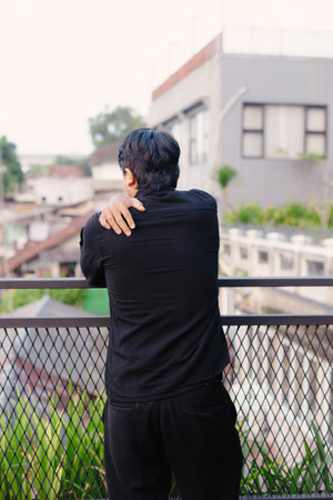 A man stands on a balcony, looking out over the urban landscape. The image captures a moment of quiet reflection. The soft light and muted tones give a sense of introspection, portraying a calm andの写真素材