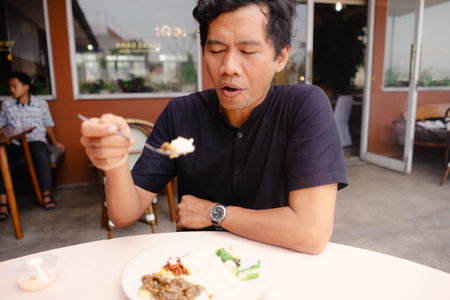 A man is engrossed in enjoying his meal at a restaurant, the focus is on the flavors and the food experience, showing satisfaction and enjoyment. The image captures a moment of culinary pleasureの写真素材