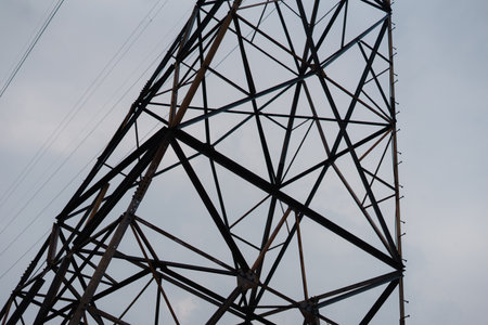 Low angle shot of a power pylon against a dull sky, the metal framework structure highlights the technology used for electricity transmission, industrial landscape.の写真素材