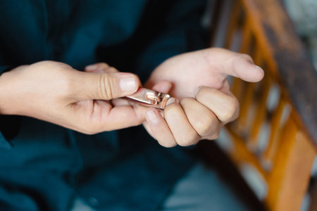 A close-up of a person's hands meticulously trimming their nails using a pair of nail clippers. The image captures the detail of personal grooming and self-care practices in a casual setting.の写真素材