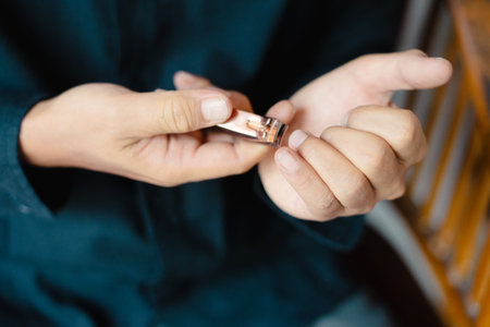 Close-up shot of a person cutting their fingernails using a nail clipper. Focus is on the hands performing a personal grooming routine, promoting cleanliness and health. The image suggests self-careの写真素材