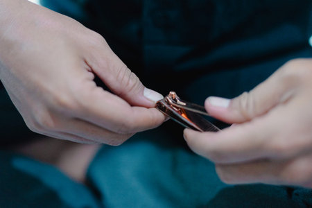 A close-up image showcases a person's hands using nail clippers to trim a fingernail. This intimate...