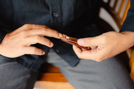 A close-up shot captures a man trimming his nails with a nail clipper, emphasizing the hands and the grooming activity. The image focuses on personal hygiene and the process of nail care in anの写真素材