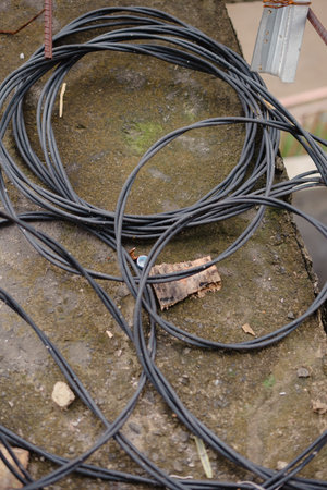 Overhead view of coiled electrical cables on a weathered concrete surface near a metal object. The...