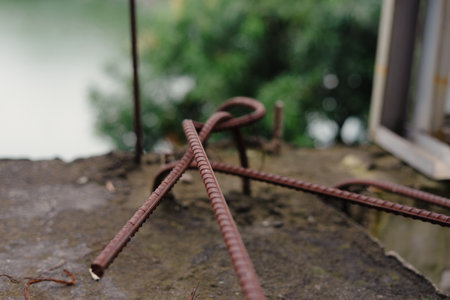 An abstract image featuring rusty rebar on a concrete surface with a blurred natural backdrop, conveying an industrial and weathered aesthetic, it depicts details of constructionの写真素材