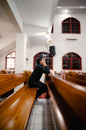 A person sits on a wooden pew, looking up in a contemplative pose within a light-filled interior space, evoking a sense of peace and reflection on a serene afternoon.の写真素材