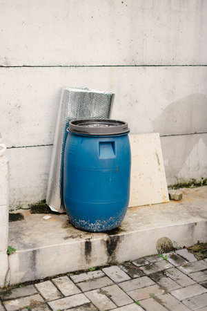 A striking image showcasing a blue plastic barrel, the central focus, positioned against a textured concrete wall, creating a contrast between the industrial and the utilitarian. The scene suggestsの写真素材
