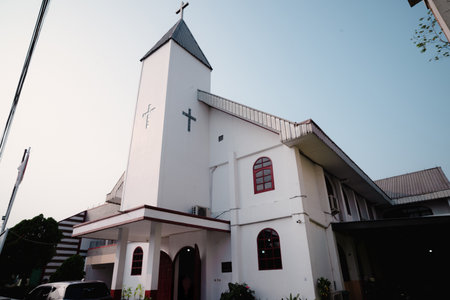 A photograph showcasing a pristine white church building under a clear blue sky. The architecture features a prominent steeple with a cross, indicative of faith and worship. The scene evokesの写真素材