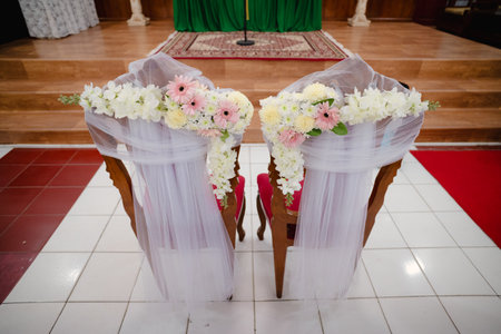 Two ornate chairs adorned with flowers and fabric are prepared for a wedding ceremony in a church. The decor sets a tone of romance and celebration, ideal for a special event or a wedding-relatedの写真素材