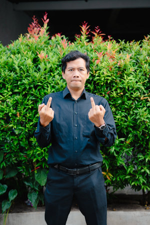 A man displays a gesture with both hands. The person's frustration is visually conveyed against a background of greenery. The expression suggests disapprovalの写真素材