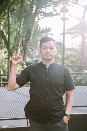 Portrait of a man pointing his index finger upward. The photo was taken outdoors with tropical foliage in the background.の写真素材