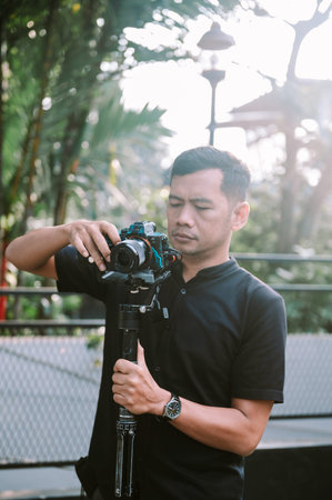 A photographer wearing a black shirt carefully adjusts his camera mounted on a gimbal, preparing for...