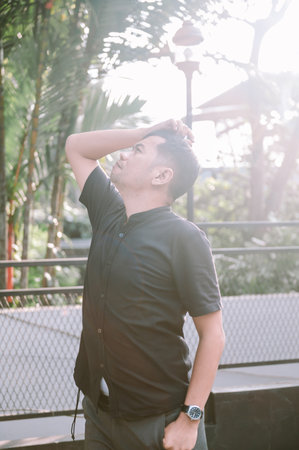 A man in a black short sleeve shirt is seen looking upwards in an outdoor setting with trees and sunlight.の写真素材