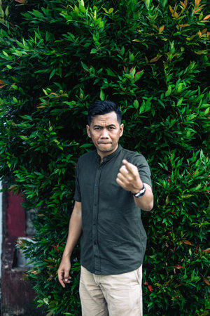 An adult man stands outdoors, gesturing with a serious expression, near dense green foliage.の写真素材