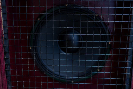Close-up of a powerful dark audio speaker, protected by a square metal mesh grill, set within a rustic dark red cabinet. Ideal for music, sound, and technology themes.の写真素材