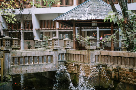A serene outdoor setting featuring a weathered stone bridge adorned with traditional pagoda-style...