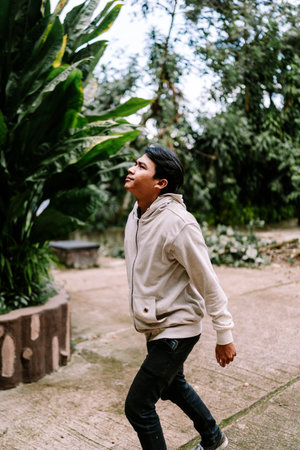 A thoughtful young man gazes upwards at the vibrant green foliage while walking casually outdoors. He is enjoying the peaceful natural environment.の写真素材