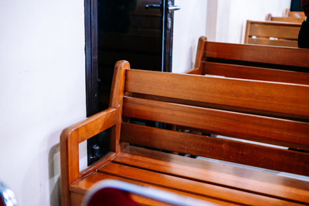 A close-up view of a row of traditional wooden benches with warm brown tones, suggesting an old church, waiting area, or assembly hall. The focus is on the rustic wood grain and repetitive pattern.の写真素材
