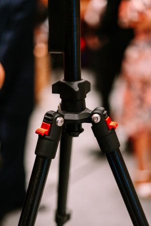 Close-up of a sturdy black photography tripod base with bright red locking levers. This essential equipment is used for stable camera support in various professional and amateur settings.の写真素材