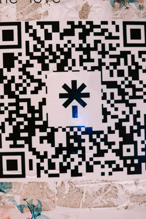 A modern QR code with a unique asterisk symbol is prominently displayed on a distressed, textured urban wall. It represents digital information, connectivity, and technology in an everyday urbanの写真素材