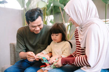 A happy Asian family, including parents and their young daughter, are enjoying creative playtime indoors. They are focused on building colorful shapes with magnetic construction toys, fosteringの写真素材