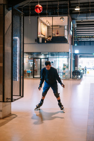 A young man wearing inline skates and protective gear actively glides through a modern indoor space,...
