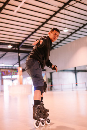 Dynamic portrait of an athletic man enjoying inline skating on a smooth indoor surface. He wears...
