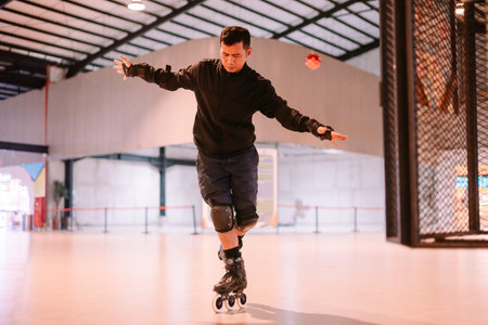 A focused man expertly balances on one leg while inline skating in a modern indoor facility. He wears protective gear, demonstrating skill and concentration during his practice session.の写真素材
