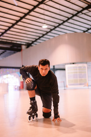 A focused man in inline skates and protective gear assumes a ready stance on a smooth indoor roller...