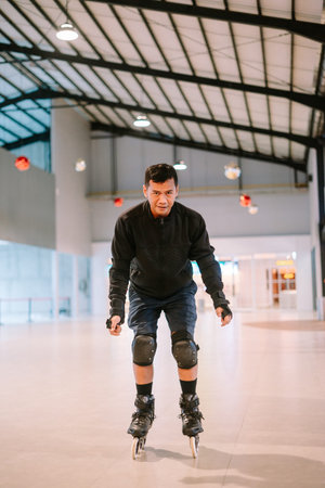 A determined man inline skating indoors, wearing protective knee pads and wrist guards. He is...