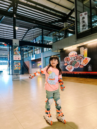 A focused little girl in protective gear and inline skates stands ready to move. She is learning to...
