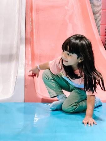 A happy young girl is enjoying herself while playing on a vibrant indoor playground with colorful slides and a soft blue floor. She smiles, engaging in fun activity.の写真素材