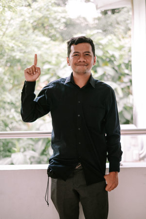 A friendly man in a dark shirt points his index finger upwards, conveying an idea or showing...