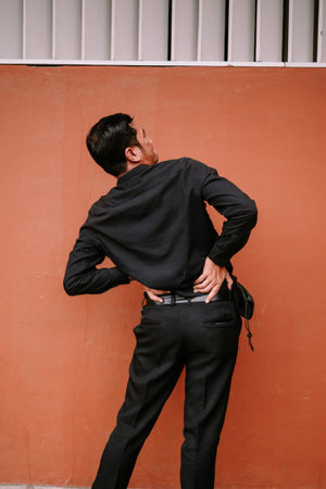 A man in a black shirt and pants is seen from behind, clutching his lower back, suggesting he is...