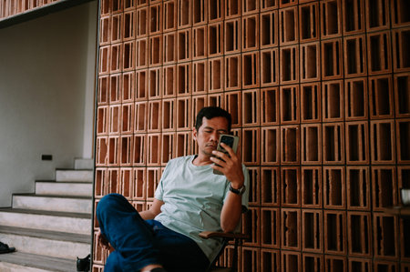 A man sits comfortably, engrossed in his smartphone, against a stylish background of terracotta...