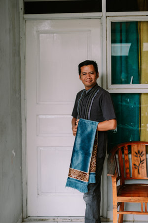 A man of Southeast Asian descent stands confidently in a doorway, holding a beautifully patterned...