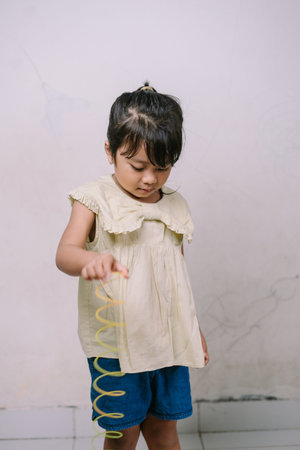 An adorable young child intently plays with a vibrant yellow spiral toy, showcasing innocent...