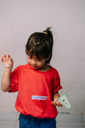 An adorable young Asian girl is deeply focused on playing with a colorful spring toy and a...
